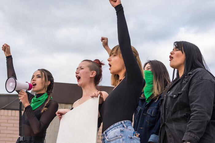 Women protesting with raised fists and a megaphone, symbolizing comments from women that make men plan their escape.