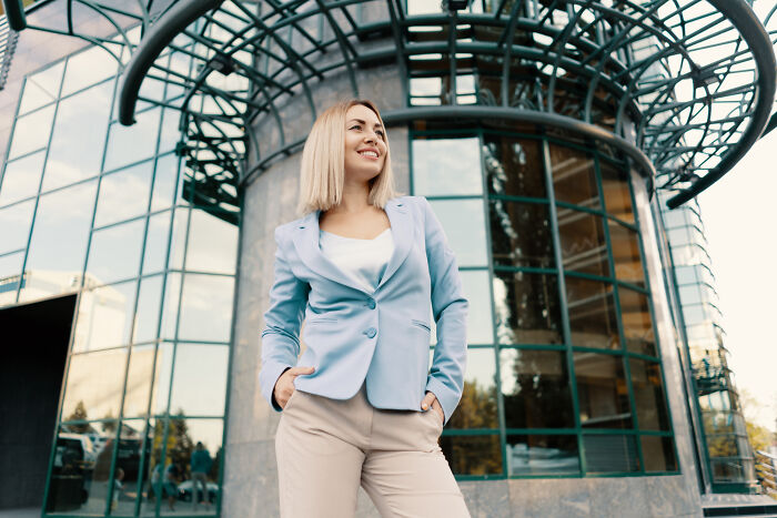 A woman smiling in front of a modern building, possibly reflecting comments from women about men planning their escape.