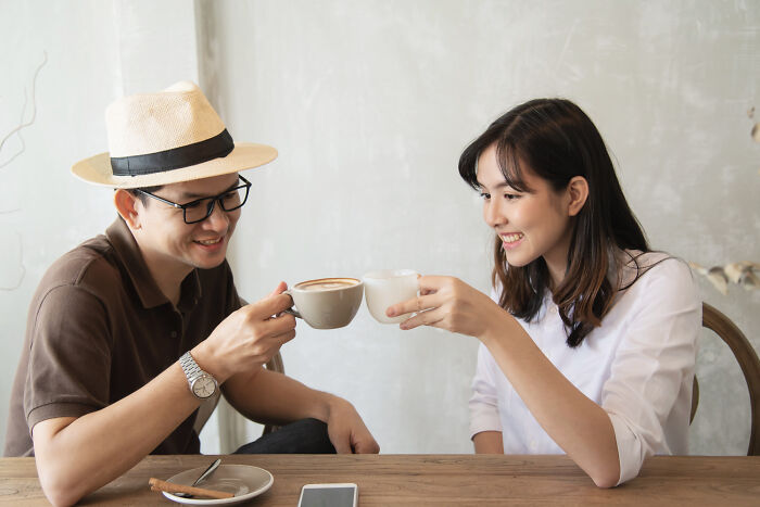 A man and a woman clinking coffee cups, smiling, perhaps planning date nights.