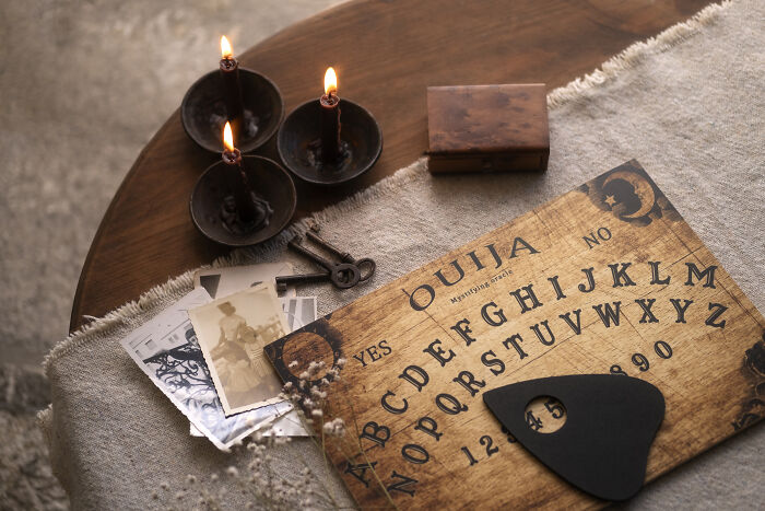 An ouija board, lit candles, old photos, and keys on a table, symbolizing a sign from the universe and spiritual connection.