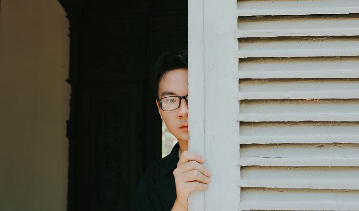 A man with glasses peeking from behind a white shutter. Women share what they put up with before walking away.