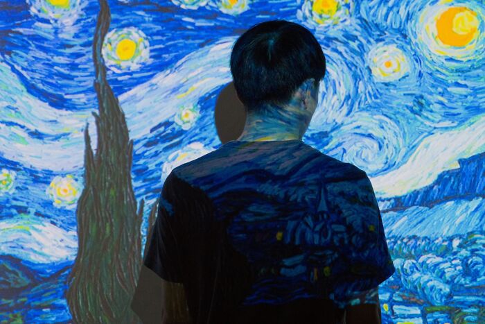 A person with their back to the camera, illuminated by a starry night projection, thinking about the worst things women endure.