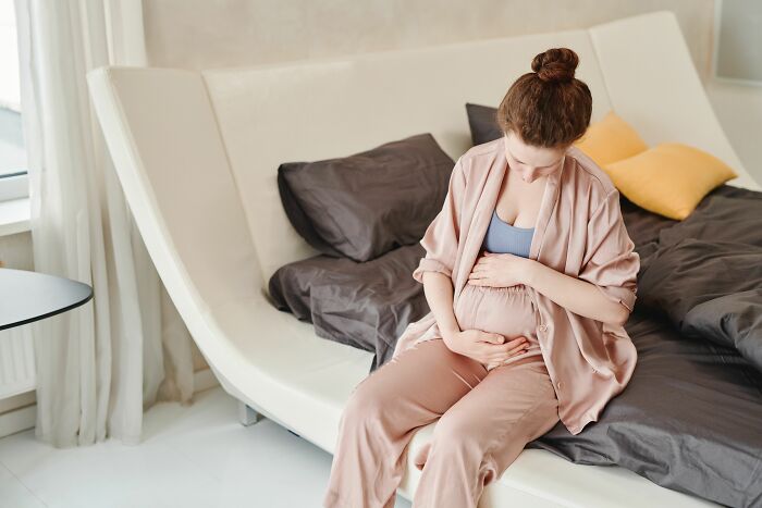 Pregnant woman sitting on a bed, holding her belly, reflecting on worst things before walking away.