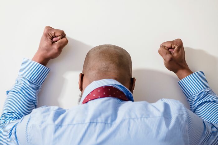 A man with his back to the camera, fists clenched against a wall, showing frustration women experience before walking away.