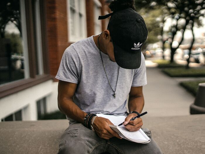 A young man in a cap writes in a notebook, possibly reflecting on the worst things women put up with.