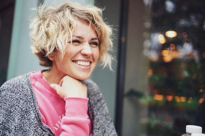 A smiling woman with short blonde hair and a pink shirt, looking happy, representing a young and dumb decision.