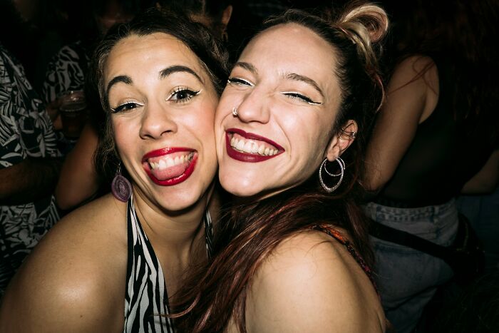 Two women with bold makeup smile and pose closely, representing a youthful and dumb decision.