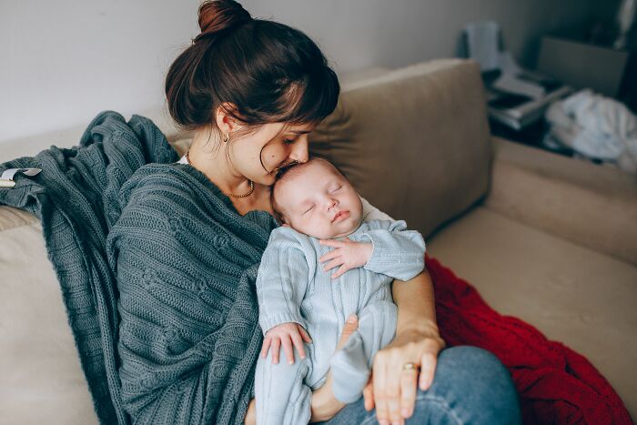 A mother holding a sleeping baby, pondering a young and dumb life decision.