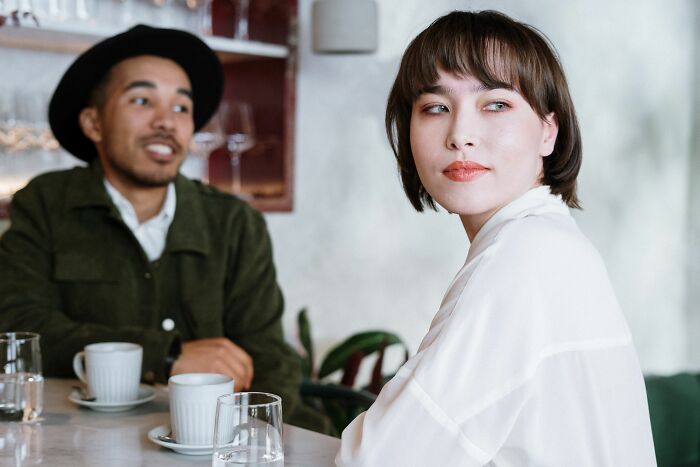 A woman looking away from a man at a cafe, reflecting on a young and dumb decision.