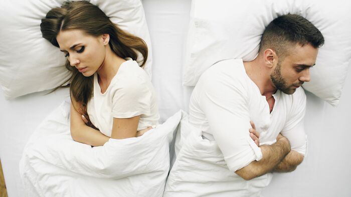 A couple lying in bed, turned away from each other, thinking about a young and dumb decision.