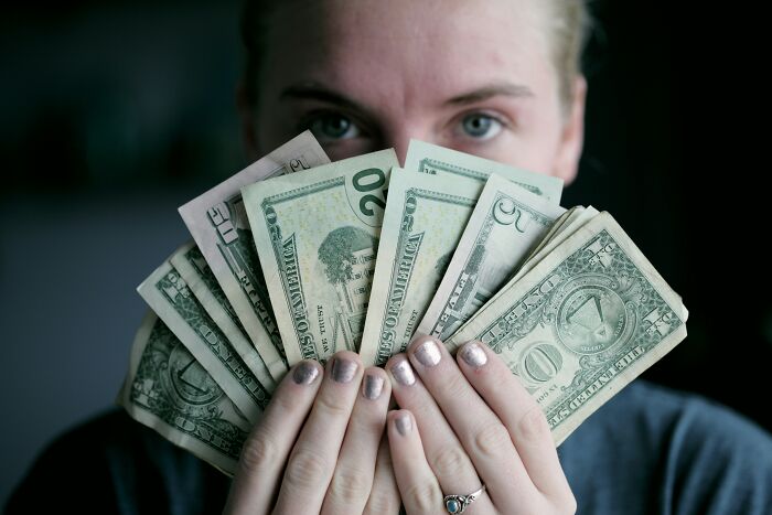 A woman holding a fan of dollar bills, representing a young and dumb financial decision.