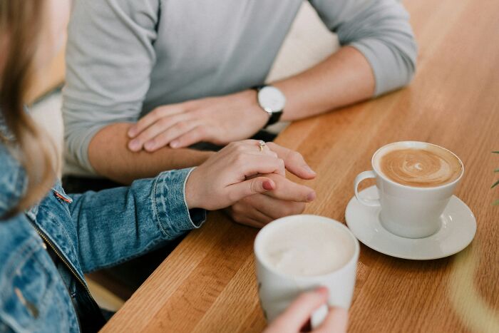 Two people holding hands over coffee, reflecting on a young and dumb decision.