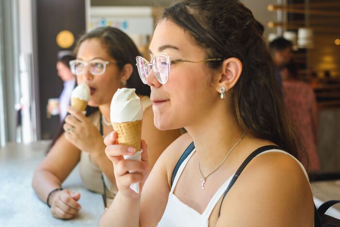 Two women wearing glasses eating ice cream cones, embodying unhinged house rules around treats or meals.