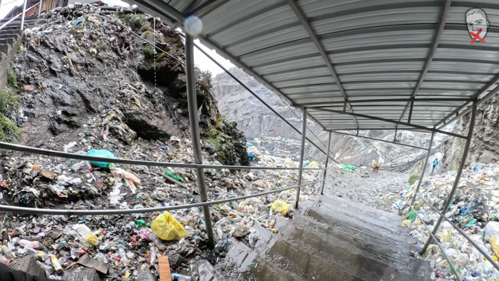 A steep, trash-strewn path in a city above the clouds, illustrating the environmental challenges and harsh conditions.