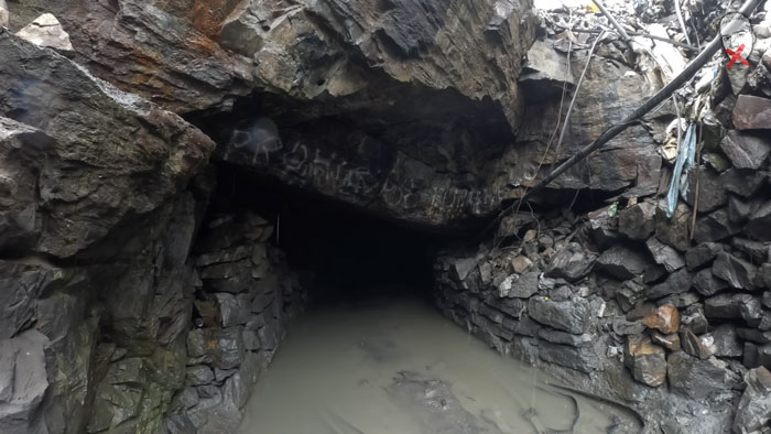 A YouTuber exploring a city above the clouds and crime, showing a dark, flooded mine entrance.