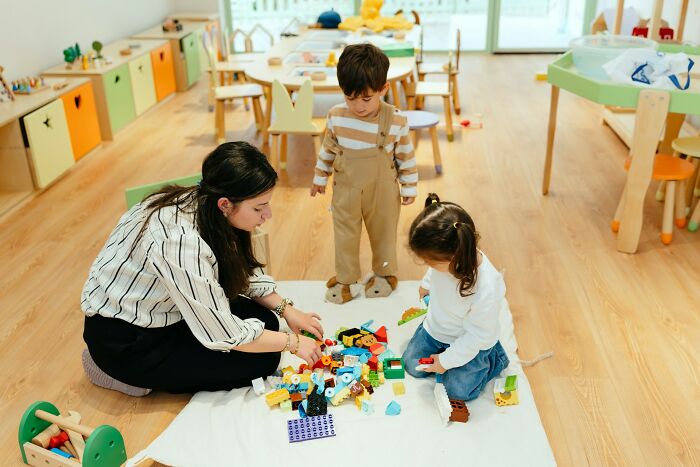 A woman playing with children and colorful blocks on the floor, reflecting poverty habits.