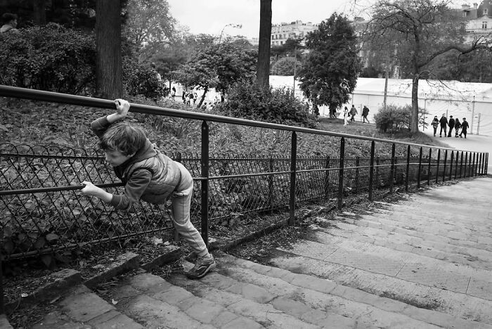A young boy clinging to a railing on a set of stairs in Paris, captured in a perfectly timed street photo.