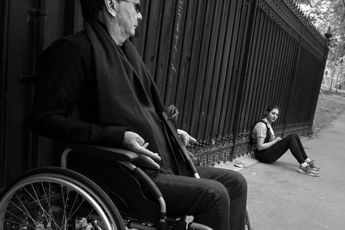 A man in a wheelchair and a woman resting on the ground, capturing a perfectly timed street photo in Paris.