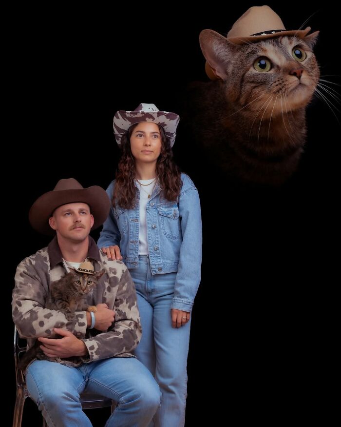 Silly portrait of a couple in cowboy hats and denim, with their cat wearing a matching hat, against a dark background.