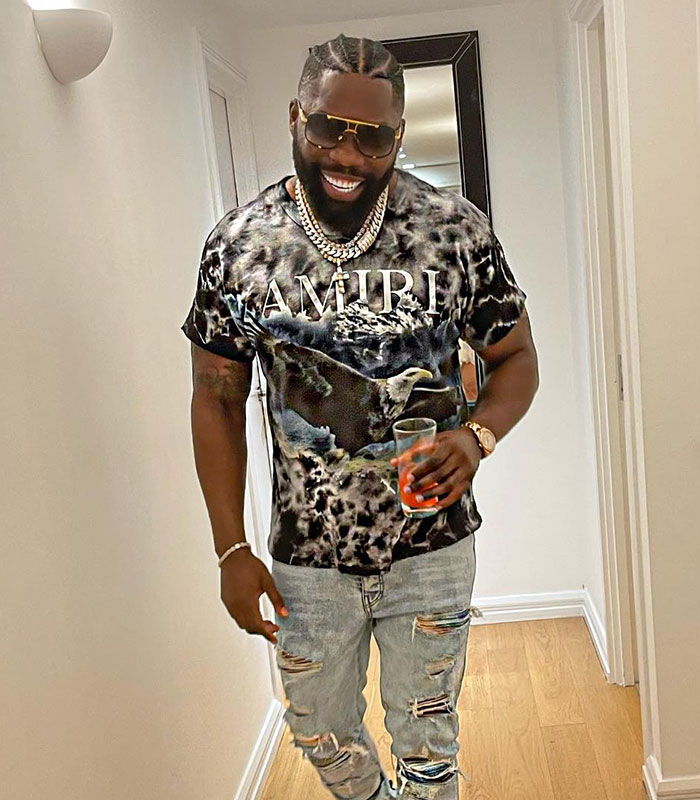 Influencer smiling, holding a drink, wearing ripped jeans and a graphic tee after a male cosmetic procedure.