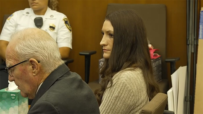 Lindsay Clancy, a woman with long dark hair, appears in court, looking to her right while a male attorney sits in the foreground. Lindsay Clancy, a woman with long dark hair, appears in court, looking to her right while a male attorney sits in the foreground.