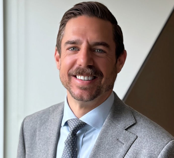 A smiling man, believed to be the Putney Pusher, in a light blue shirt and gray suit jacket.