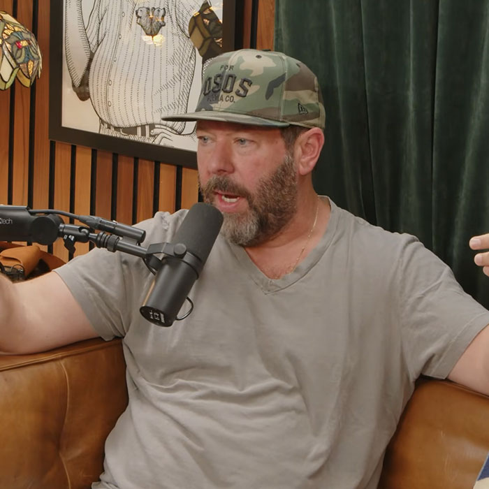 Bert Kreischer wearing a camo cap and talking into a podcast microphone. Bert Kreischer wearing a camo cap and talking into a podcast microphone.