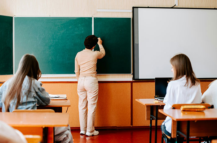 A teacher writing on a blackboard in a classroom, symbolizing a teacher's actions in a school trip scenario.