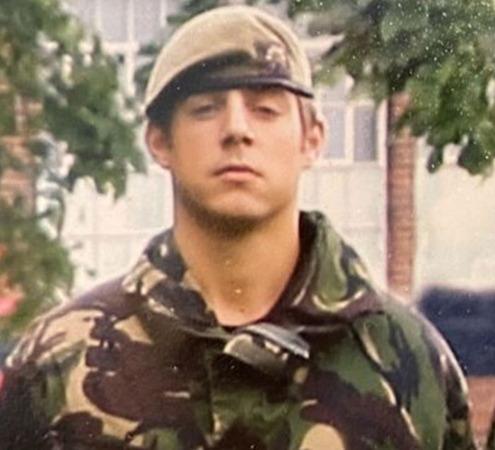 A younger man, believed to be the Putney Pusher, in military fatigues and a cap, looking serious.