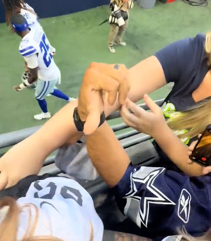 A woman reaching to grab a signed NFL hat from a young fan at a match A woman reaching to grab a signed NFL hat from a young fan at a match