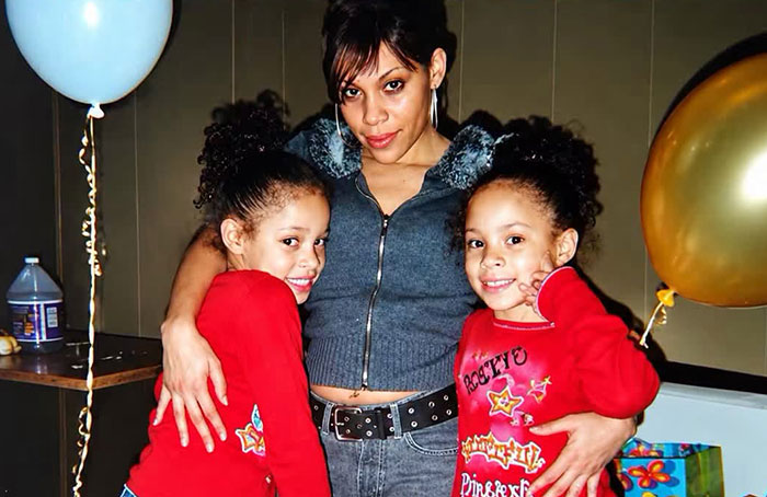 A mother posing with her young twin daughters in red shirts at a birthday party A mother posing with her young twin daughters in red shirts at a birthday party