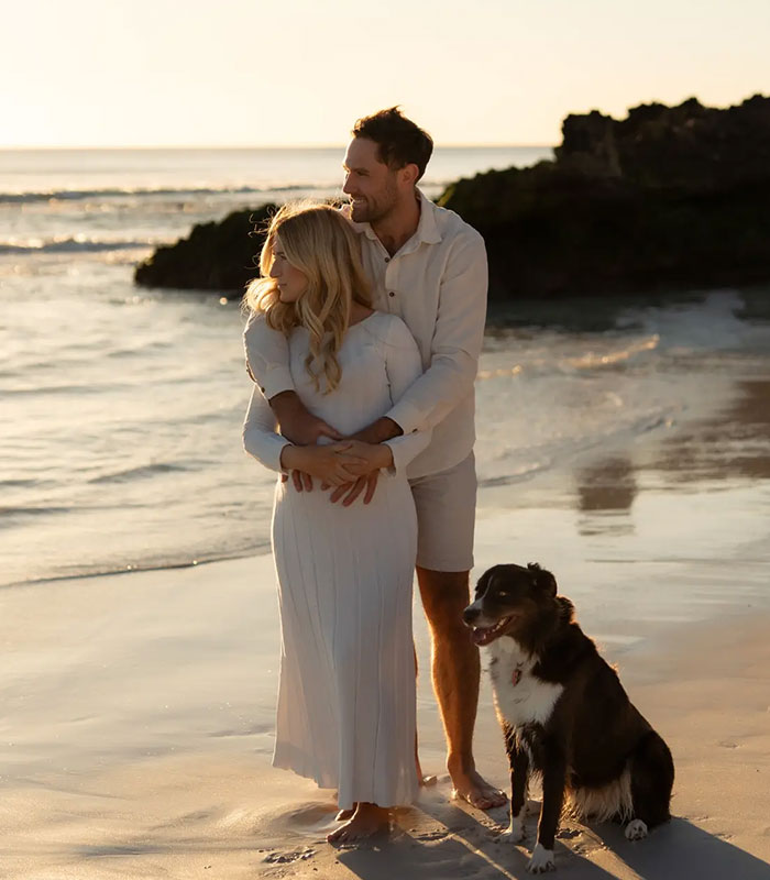 Star athlete and wife embracing on a beach at sunset with their dog
