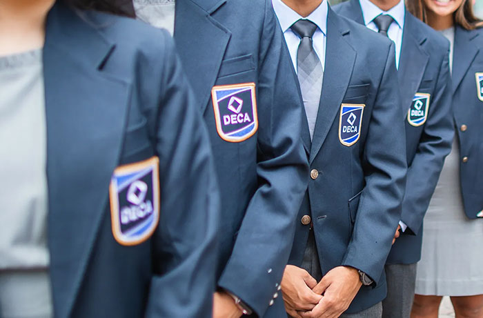 Students in school uniforms with DECA badges, representing teens on a school trip and rooming arrangements.