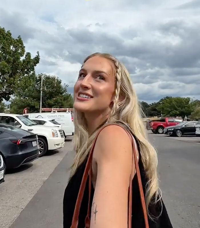 A blonde shopper looking up and smiling while standing in a parking lot.