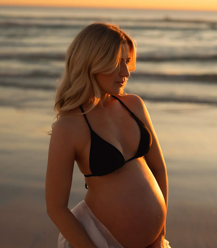 Pregnant wife of star athlete in black bikini top at sunset on the beach
