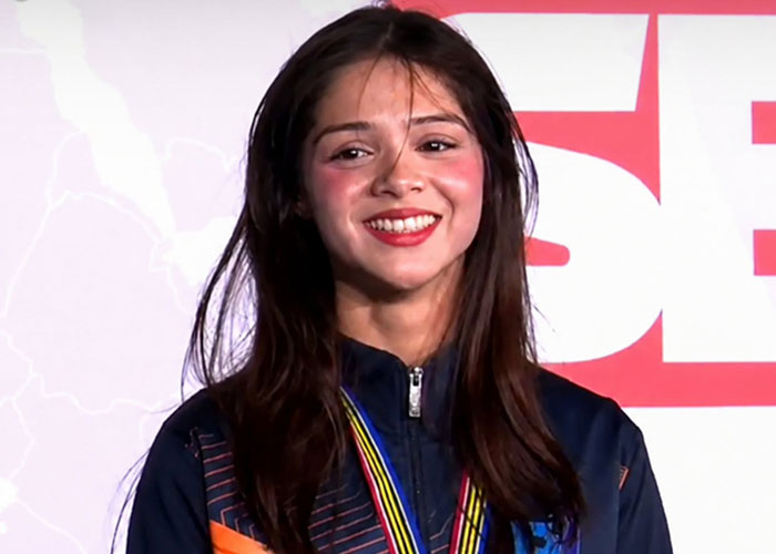 Close-up of a smiling female weightlifting medalist wearing her medal, showing her achievement despite her petite frame. Close-up of a smiling female weightlifting medalist wearing her medal, showing her achievement despite her petite frame.