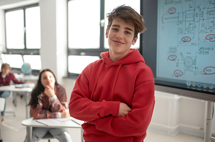 A smiling teen boy in a classroom, depicting a closeted teen possibly affected by a teacher outing them.