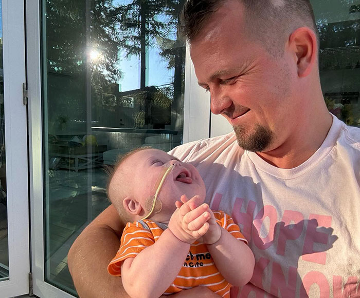 Father smiling at baby with feeding tube reflecting hospital lawsuit involving grieving parents Father smiling at baby with feeding tube reflecting hospital lawsuit involving grieving parents