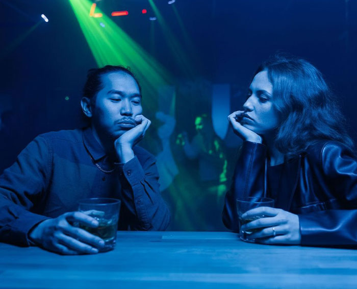 A bored man and woman sitting at a bar under neon lights, illustrating common dating mistakes. A bored man and woman sitting at a bar under neon lights, illustrating common dating mistakes.
