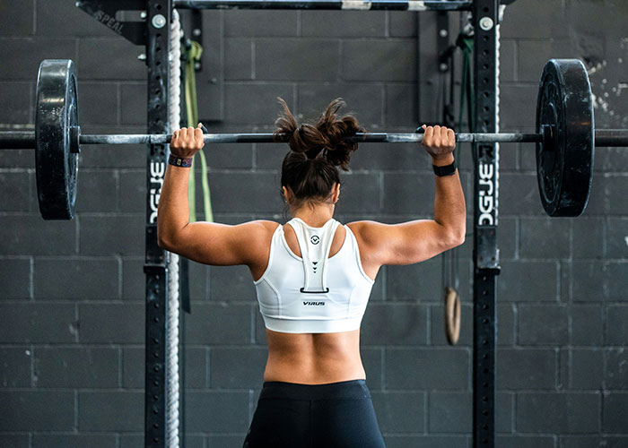 A female weightlifting medalist performing an overhead lift with a barbell at the gym, showcasing her petite frame. A female weightlifting medalist performing an overhead lift with a barbell at the gym, showcasing her petite frame.