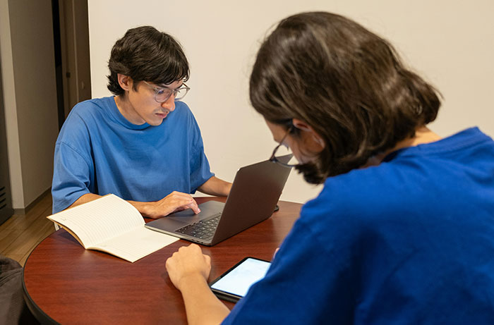 Two teens studying together with a laptop, reflecting rooming plan issues for a closeted teen on a school trip.