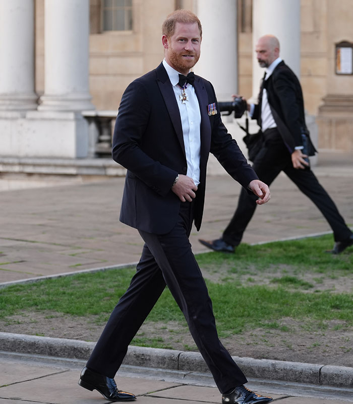 Prince Harry in a suit, walking, as discussion arises about his kids' schooling and his silence amid backlash.