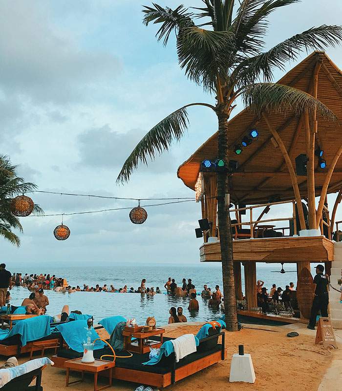 Bali beach bar with palm trees and people swimming at sunset Bali beach bar with palm trees and people swimming at sunset