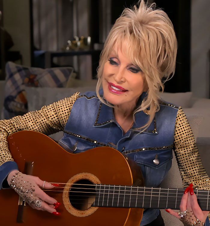 Dolly Parton playing guitar in a final video, dressed in a denim vest with gold embellishments. Dolly Parton playing guitar in a final video, dressed in a denim vest with gold embellishments.