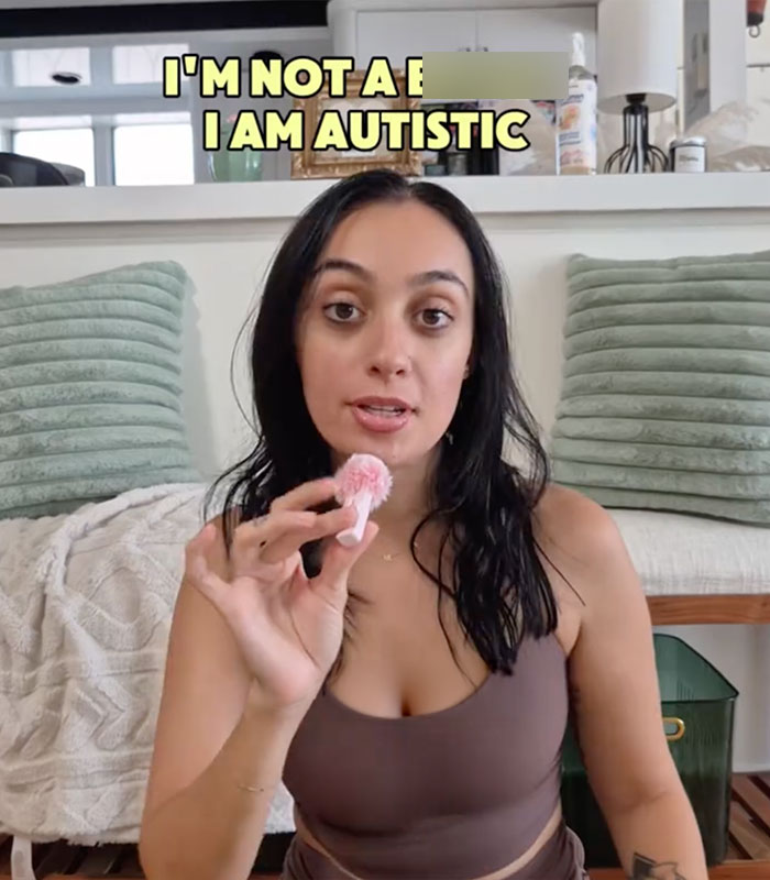 A woman with autism holding a small pink microphone, with text stating 'I'm not a b****, I am autistic'.