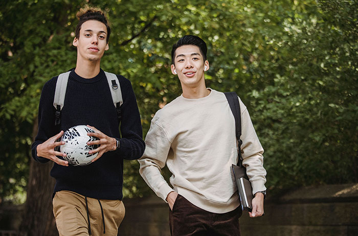 Two male teens walking together, one holding a soccer ball, enjoying a school trip.