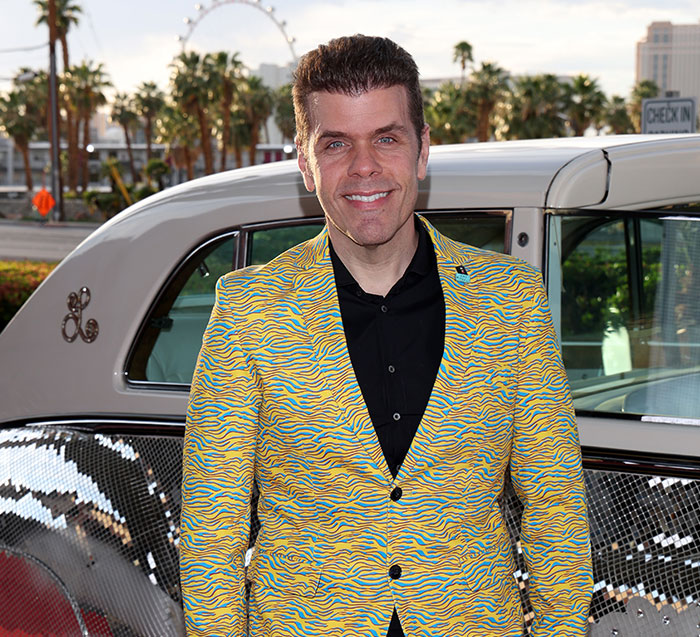 Perez Hilton smiling in a yellow and blue tiger-print jacket.
