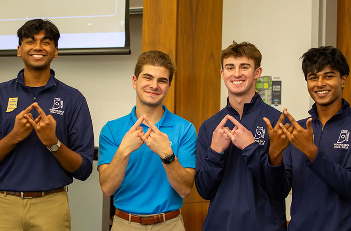 Four male teens making hand gestures, possibly on a school trip.