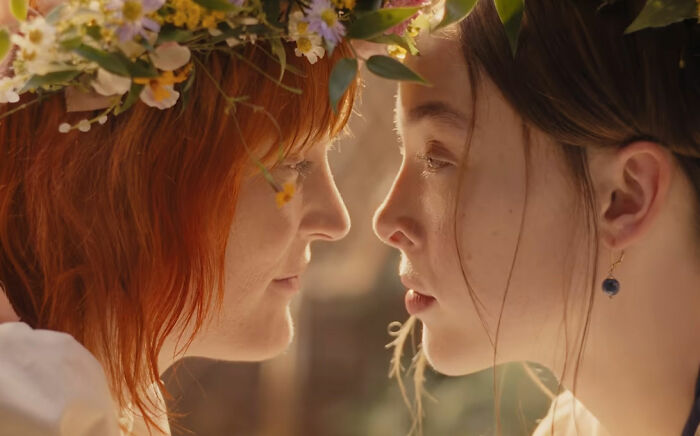 Two women with floral wreaths, facing each other with intense expressions in a scene from the nepo baby's show.