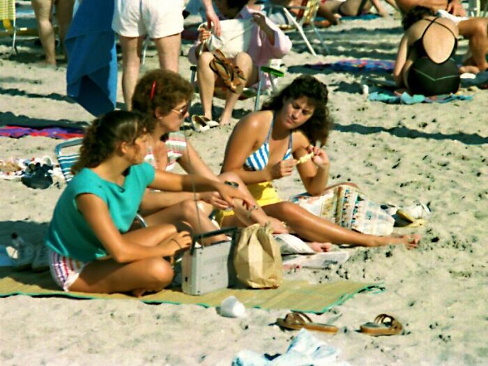 Three women on a beach enjoying their 80s retro tech, a portable radio, capturing the glorious weirdness.